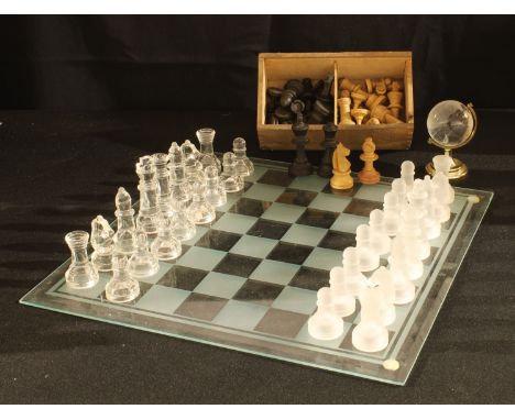 A carved wooden chess set in a wooden box with sliding cover; a glass chess set and board; a glass desk globe (3) 