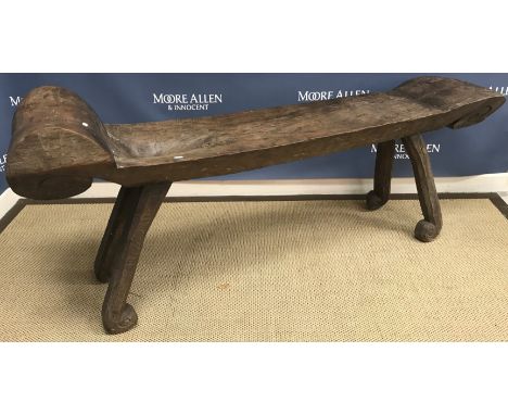 An Indonesian rustic wooden sleeping bench with scroll head rest and shoulder recess and scrollwork foot end, raised on splay