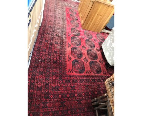 An Afghan rug, the central panel set with repeating medallions on a dark red ground within a red and black scrolling stylised