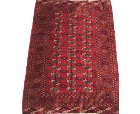 A Bokhara Tekke rug, the central panel set with three repeating rows of stylised elephant foot medallions on a red ground, in