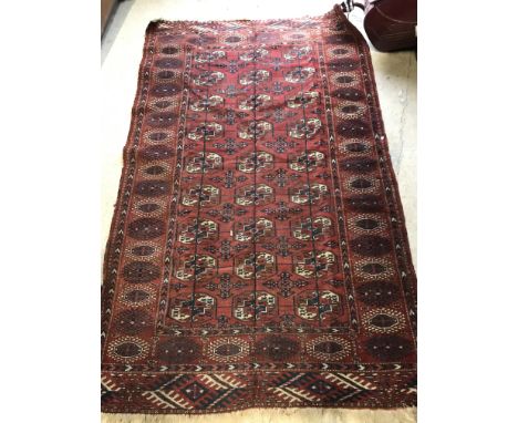A Bokhara rug, the central panel set with repeating elephant foot medallions on a red ground, within a stepped red, cream and