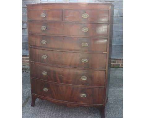 An early 19th century figured mahogany bowfront chest of two short and five graduated long drawers with oval brass handle pla