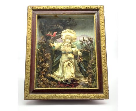 Cased clockwork automaton doll wearing a silk dress in a naturalistic garden setting, with paper label to the back of the cas