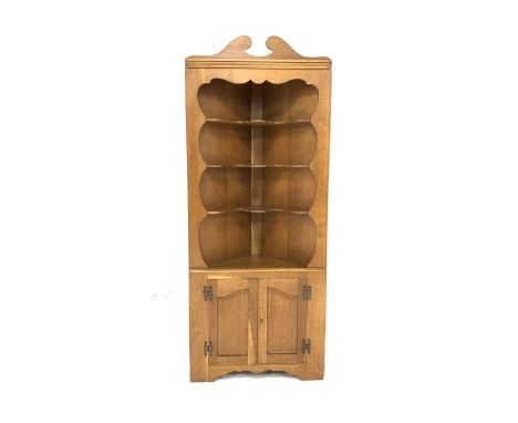 20th century light oak floor standing corner cupboard, swan neck pediment above shaped aperture enclosing three open shelves,