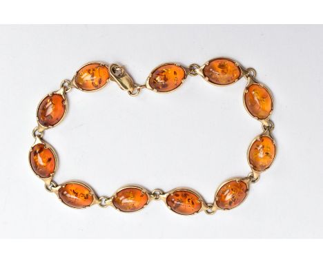 A 9CT GOLD AMBER LINE BRACELET, designed with a row of eleven oval amber cabochons, each collet mounted, interspaced with jum