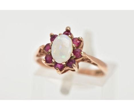 A 9CT GOLD OPAL AND RUBY RING, centring on an oval cut opal, prong set within a surround of eight circular cut rubies, leadin