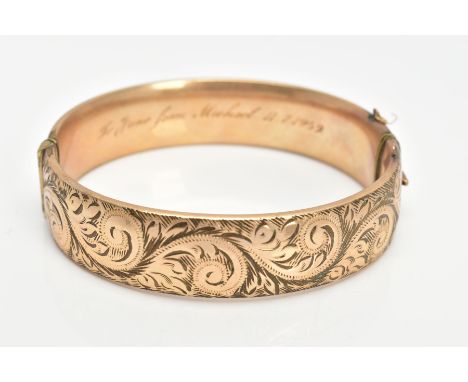 A 9CT GOLD METAL CORE BANGLE, half with a foliate scroll detail, fitted with a push pin clasp, missing safety chain, engraved