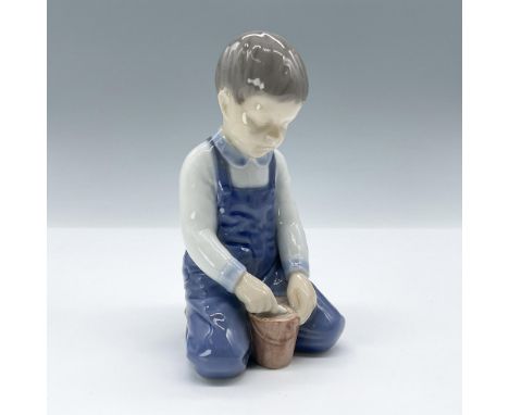 Charming porcelain figurine depicting a young boy playing with a pail. Finished in glossy underglaze technique with subtle hu