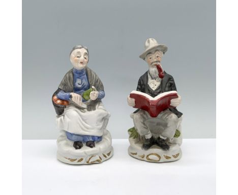 An older man seated, engrossed in a book with a pipe in his mouth, joined by his wife, also seated, delicately cutting an avo