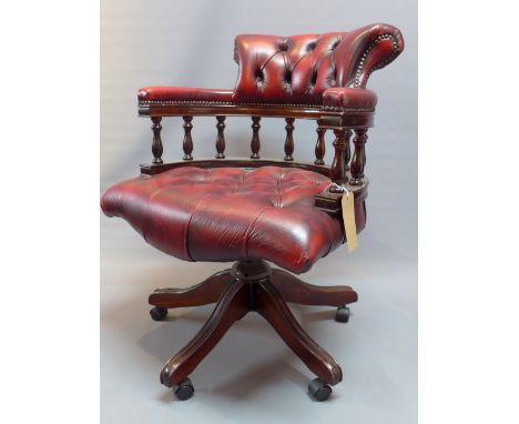 A 20th Century mahogany captain's desk chair with red leather button back upholstery, raised on splayed legs and castors. 