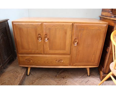 A mid Century Ercol blonde teak sideboard with a combination of three cupboards and a single drawer on four splayed legs