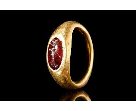 Ca. 100-200 AD.A gold ring with a rounded hoop that comes together to hold a bezel. The stone is finely carved with a right f