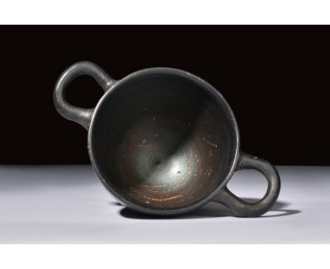 Ca. 350 BC.A black glazed skyphos with a sleek body, two curvilinear handles, and a lustrous black glaze, typical of ancient 