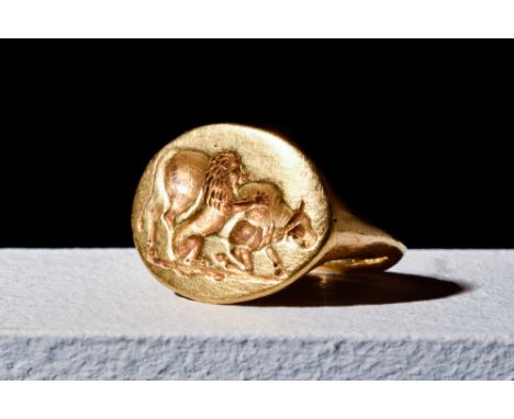 Ca. 400 BC.A gold ring with a slim rounded hoop holding a large bezel with elaborate engravings of a lion attacking a bull. S
