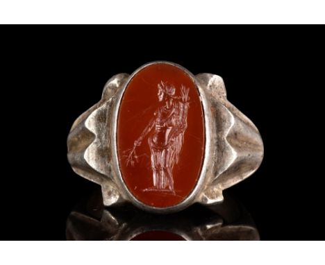 Ca. 200 AD.A silver ring with a simple circular hoop and ornate ribbed shoulders. The large bezel holds a red stone intaglio 