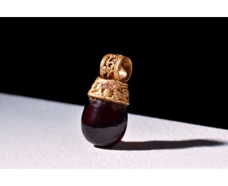 Ca. 300-100 BC.A gold filigree pendant with a circular suspension loop, leading to a flaring body in a garnet setting. Size: 