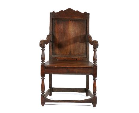 18th Century oak armchair, the arched top rail above a single panel back and solid seat flanked by curved arms above turned l