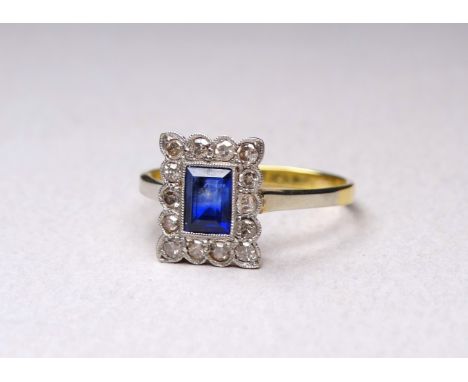 An 18ct gold sapphire and diamond set ring - in the Art Deco style, the central emerald cut stone within a band of diamonds, 