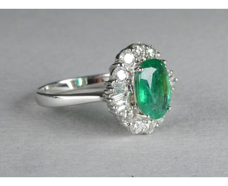 An 18ct white gold emerald and diamond ring - the central oval stone within a band of diamonds, central stone 1.79ct, size M,