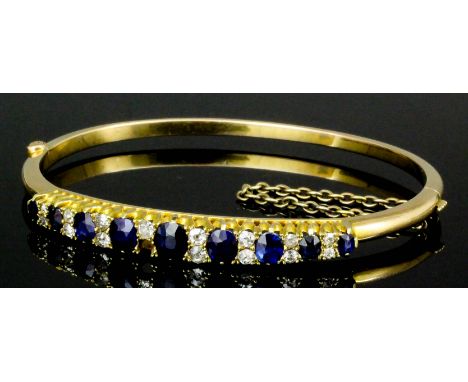 A late 19th Century 15ct gold sapphire and diamond set stiff bangle, the face set with nine oval cut sapphires, graduating fr