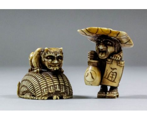 A Japanese carved ivory netsuke of Shoki and a demon, the demon seated on a large overturned basket beneath which he as trapp
