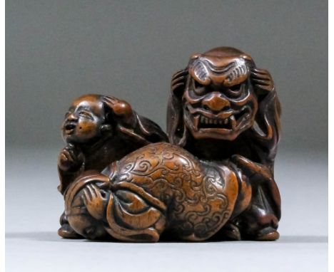 A Japanese carved boxwood netsuke in the form of two children cowering away from a standing child with a grotesque mask, 1.25