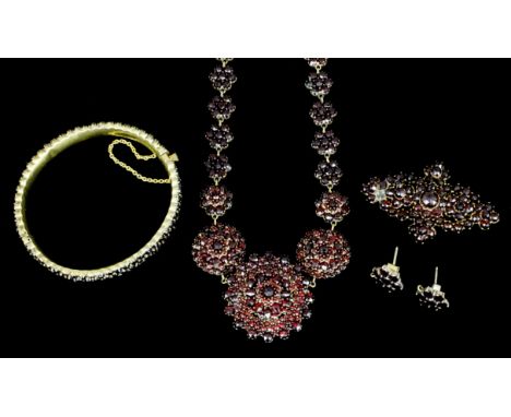 A late Victorian gold coloured metal mounted garnet set suite of jewellery, comprising - flowerhead pattern necklace set with