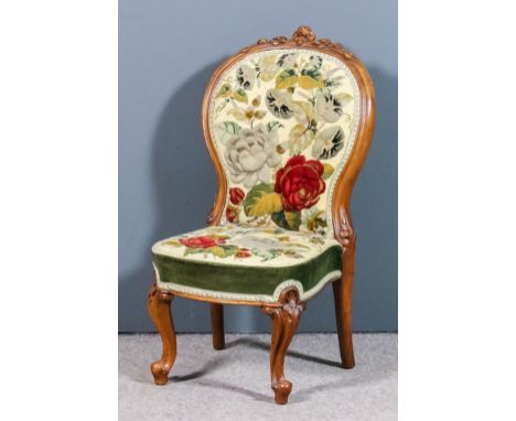 A Victorian walnut framed spoon back nursing chair, the showwood frame with floral carved cresting, the seat and back upholst