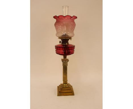 A Victorian brass corinthian column table oil lamp, having cranberry glass font and Art Nouveau foliate etched shade with cri