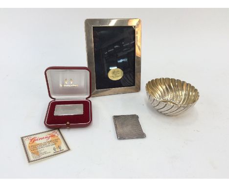 A modern silver mounted easel photograph frame; a small plated engine turned decorated card case; a cased silver ingot depict