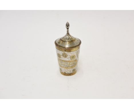 A Middle Eastern white metal cup and cover, having yellow metal overlaid decoration of flowers and Islamic script, 18cm high