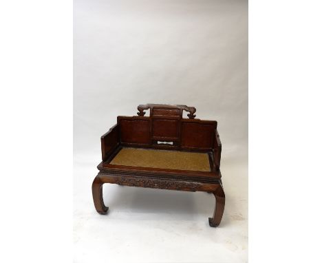 A Chinese hardwood two seat bench, having raised panel back, Hessian seat above a foliate decorated frieze and bold scroll su