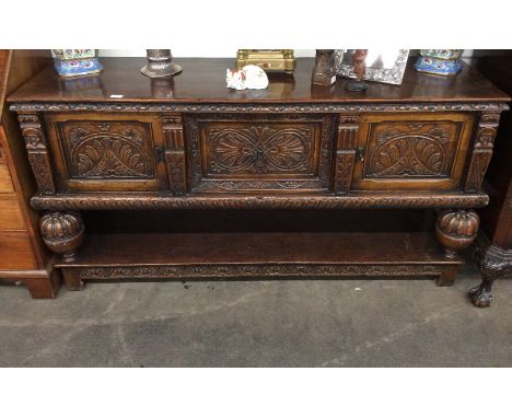 A Jacobean style reproduction oak dresser base, having profuse carved foliate decoration, central deep drawer flanked by cupb