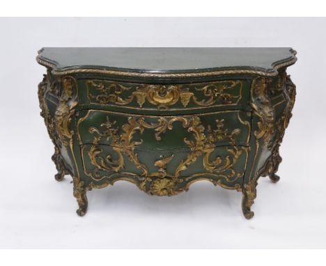 An Italian green and gilt painted serpentine fronted bombe shaped commode, fitted three drawers profusely decorated with mask