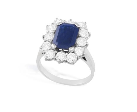 A SAPPHIRE AND DIAMOND CLUSTER RINGSet with a rectangular-shaped sapphire, within a brilliant-cut diamond surround, ring size