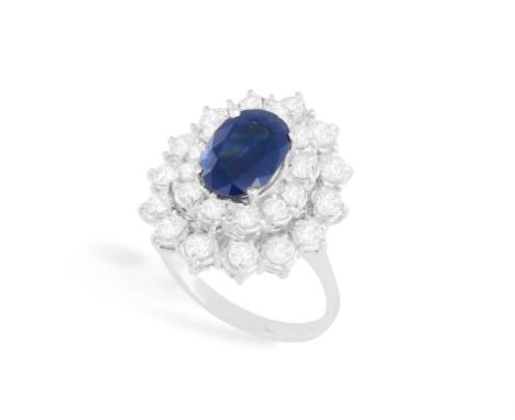 A SAPPHIRE AND DIAMOND RINGSet with an oval-shaped sapphire, within a brilliant-cut diamond double surround, to a polished ho