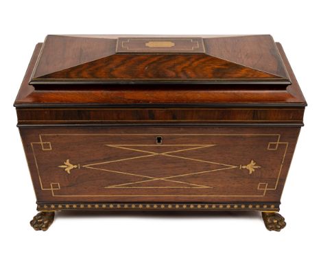 A Regency tea caddy of sarcophagus form on brass paw feet, the top opening to reveal a fitted interior with a glass bowl and 