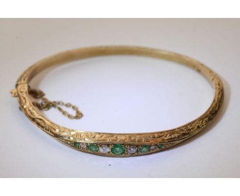 A 9ct gold diamond and emerald embossed hinged bangle.