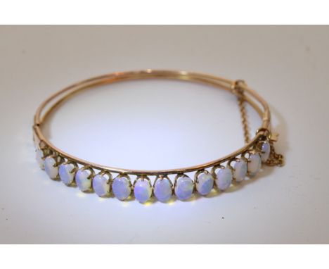 An antique hinged bangle set with 14 well matched water opals and safety chain.