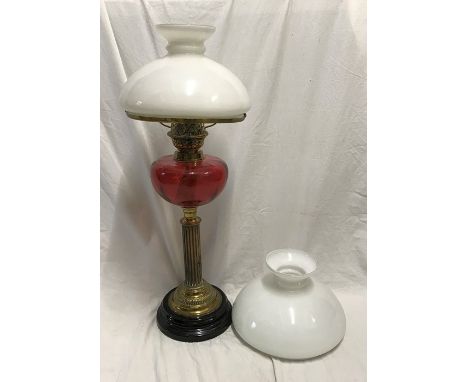 Cranberry glass oil lamp with brass corinthian column base and milk white shade, plus a spare shade, 65cms h. Condition Repor