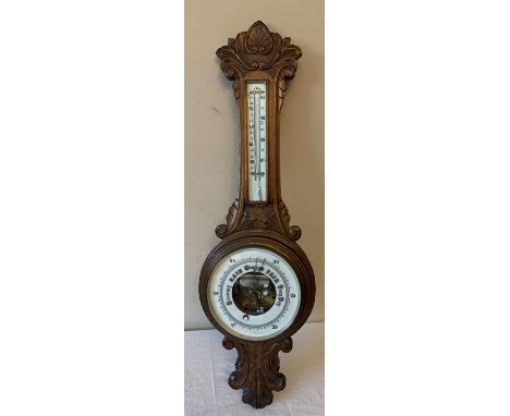 An oak cased aneroid barometer with carved body, 87cms h. Condition ReportGood condition apart from thermometer come away fro