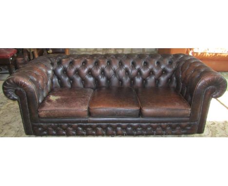 A traditional three seat brown leather upholstered Chesterfield sofa with button finish and loose seat cushions (one cushion 