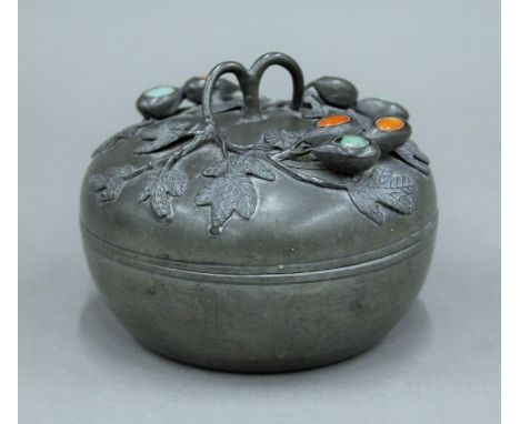 A 19th century Chinese circular pewter box, the lid decorated with applied trailing leaves and fruit with inset green jade an
