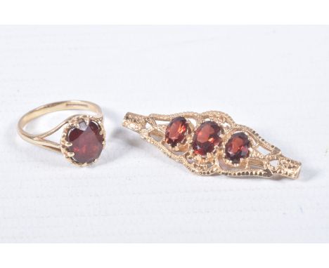 A 9CT GOLD RING AND YELLOW METAL BROOCH, an oval cut garnet, prong set in yellow gold leading on to trifurcated shoulders, ha