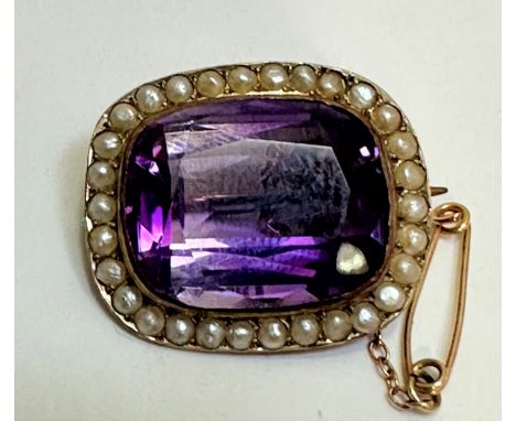 An Edwardian 9ct gold brooch set cushion cut faceted amethyst in rub over mount enclosed within a border of half seed pearls,