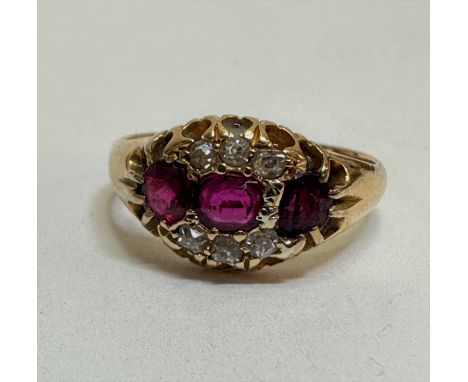 An 18ct gold three stone ruby and diamond ring, the oval cut stone flanked by a circular circular cut ruby with three old cut