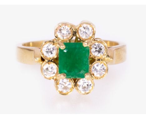 An emerald and diamond oval cluster ring, the rectangular step cut emerald four claw set and surrounded by eight brilliant cu