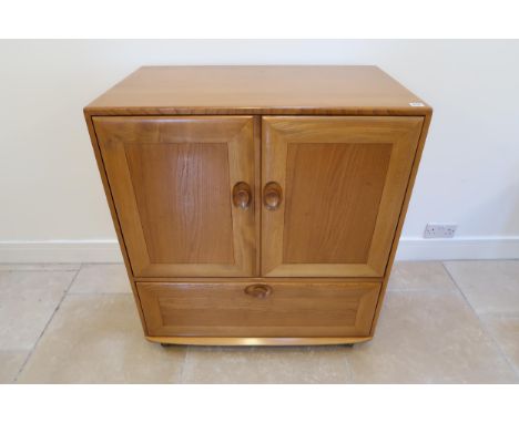 An Ercol blonde elm mid 20th Century cabinet of two doors, single fall from below with sliding tray to base raised on casters