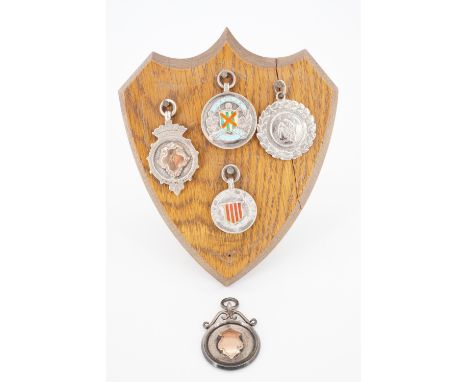 Five vintage silver prize fob medallions presented on an oak shield-shaped display with easel back, including 193-40 West Tyn