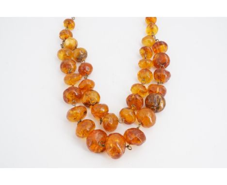 A vintage Latvian amber necklace, with two strands of graded polished beads, on a base metal chain, largest bead 25 x 20 mm, 